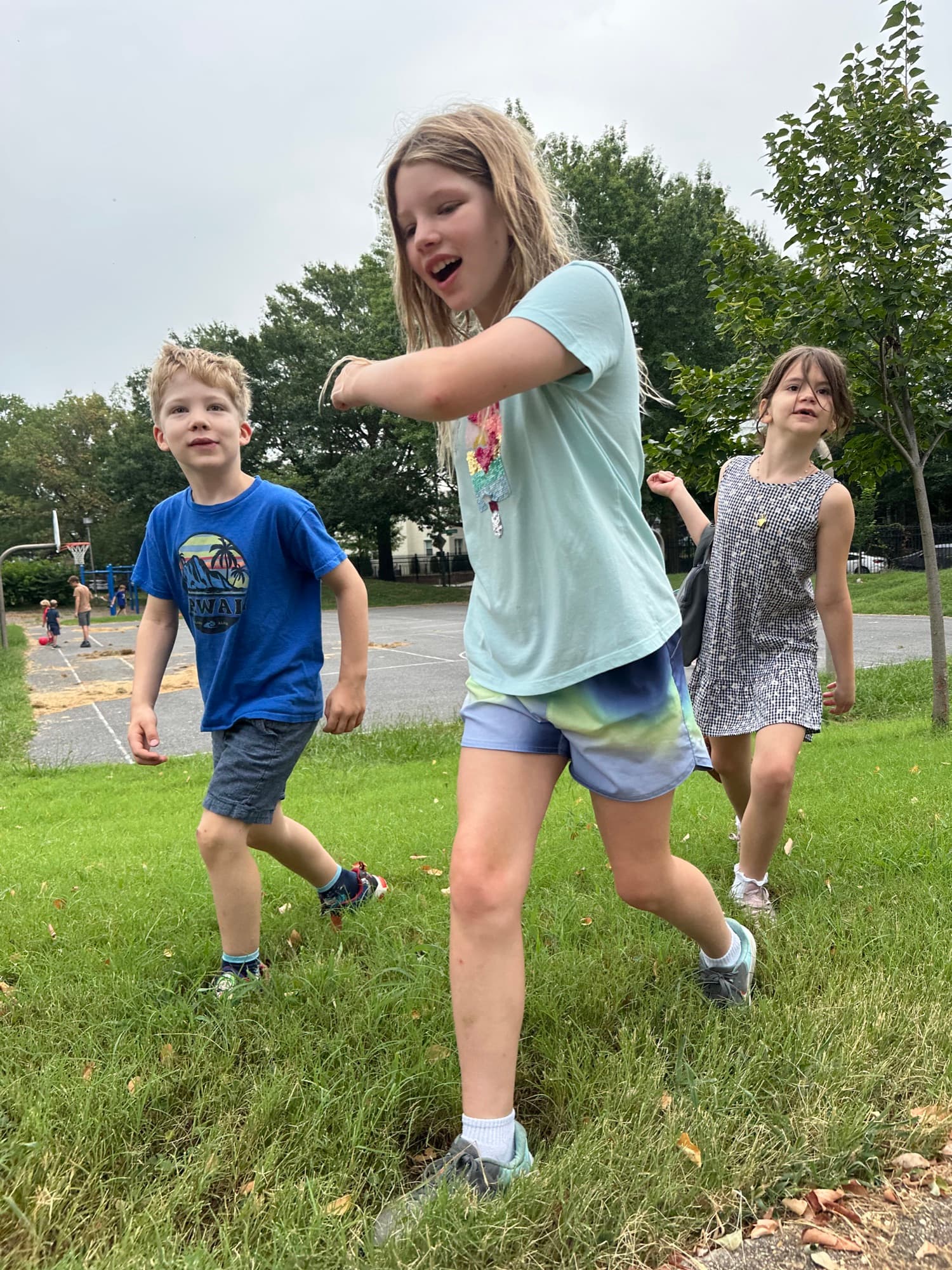 Three children playing outside on a grassy area near a playground
