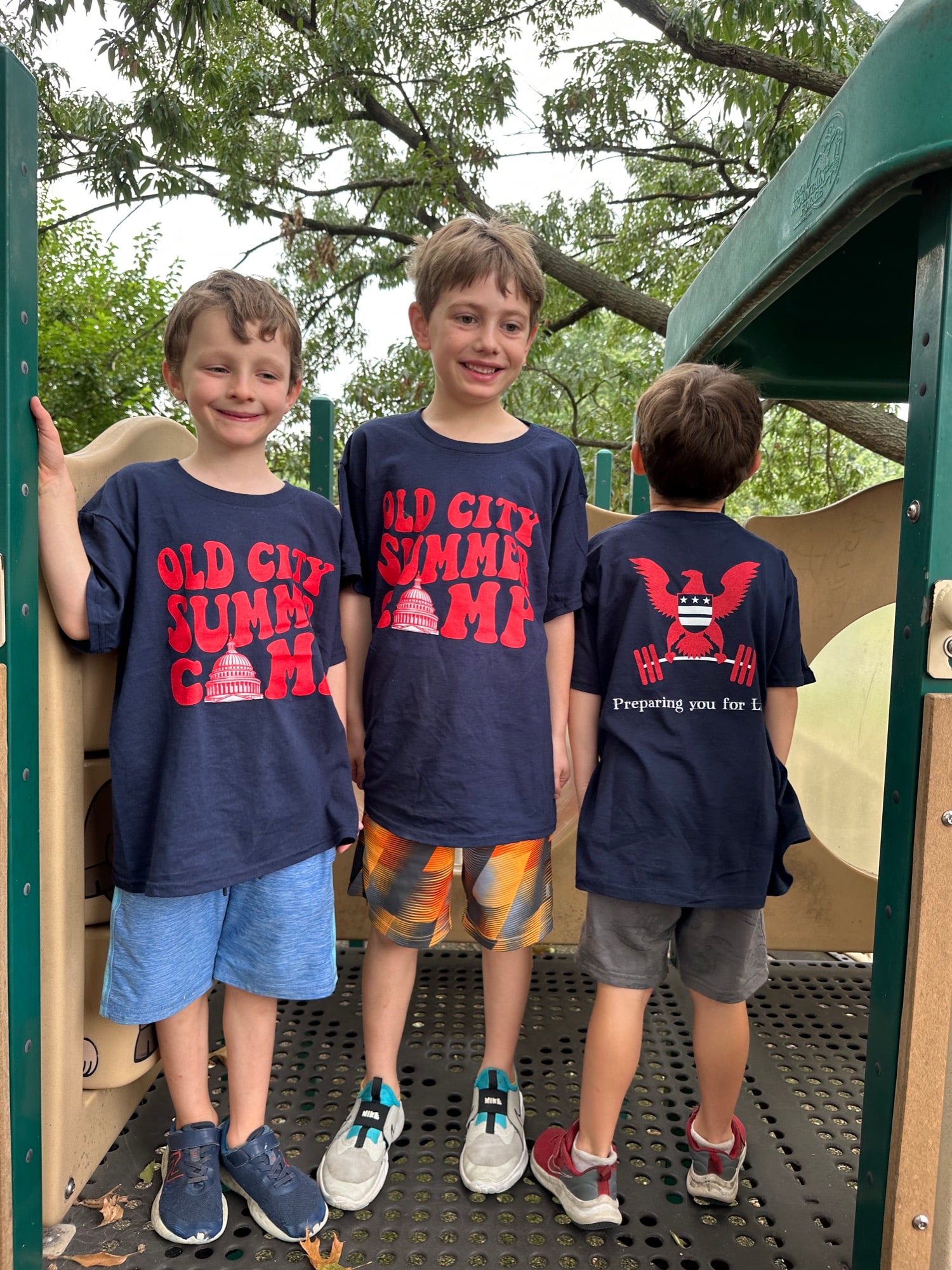 Three campers in matching navy Old City Kids shirts on a playground structure