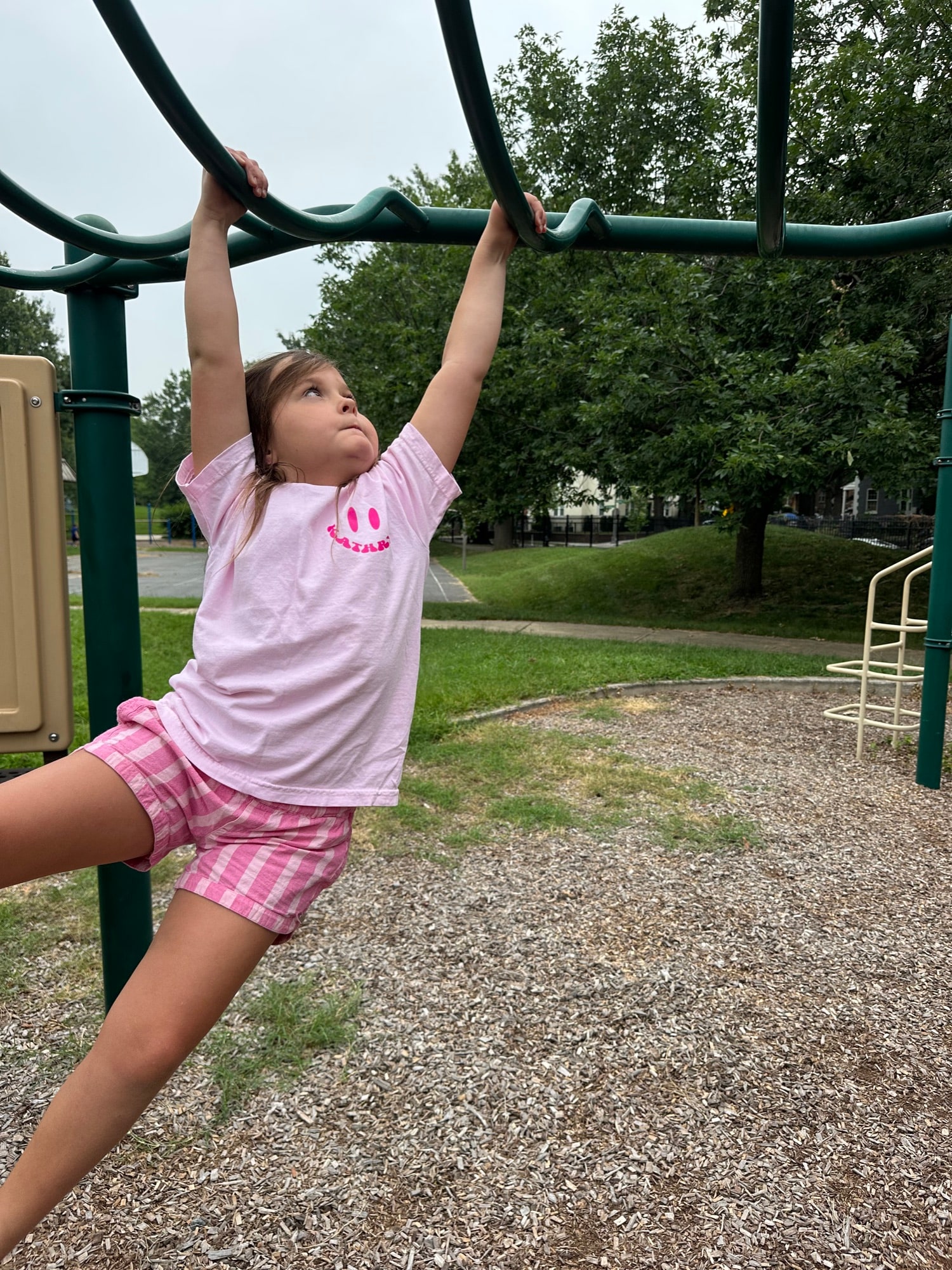 A girl hanging from playground bars at the park